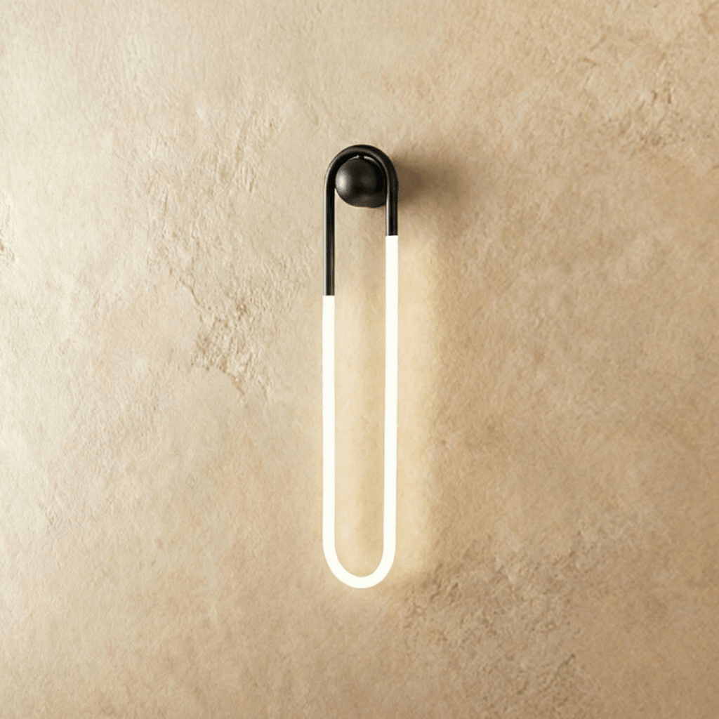 Clérachic slim U-shaped wall light with a matt black arch and ball mount and a glowing frosted tube, on limewash plaster.