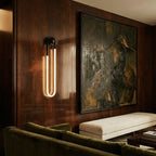 Clérachic black U-shaped wall light glowing on a polished walnut-panelled wall near a large painting, bench and olive sofa.