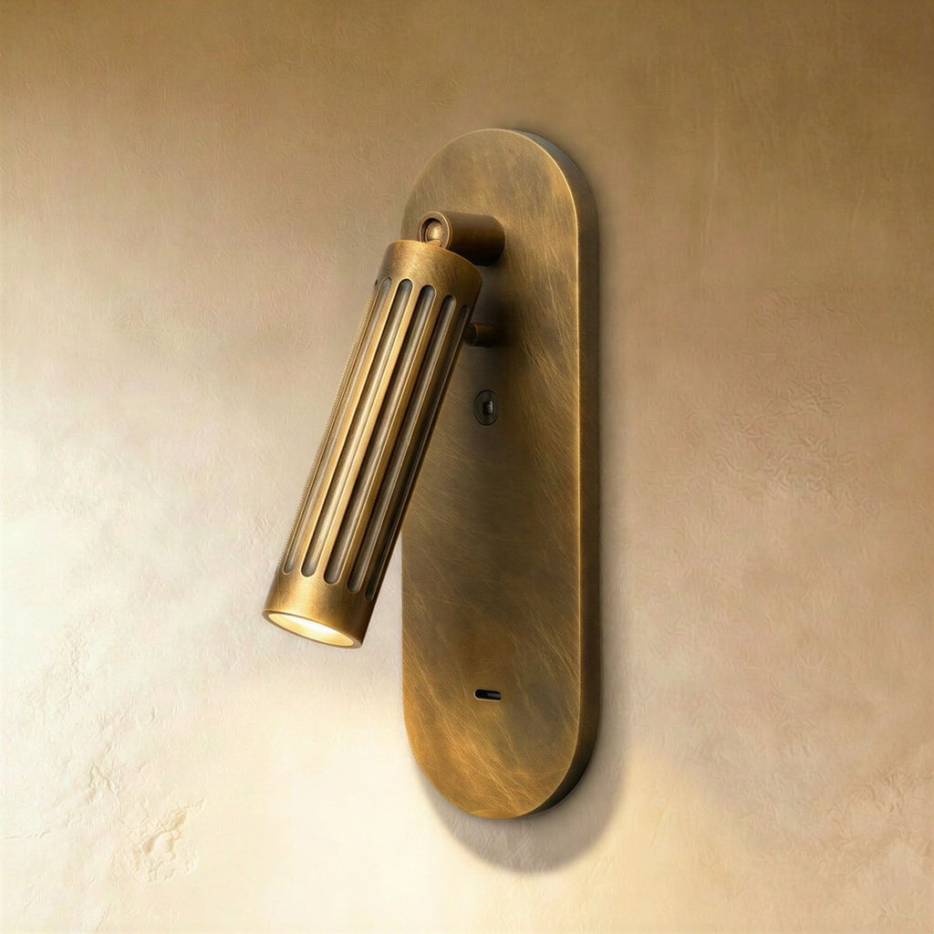 Clérachic fluted brass wall light with a tilted cylindrical head, lit warm on a slim oval backplate against plaster