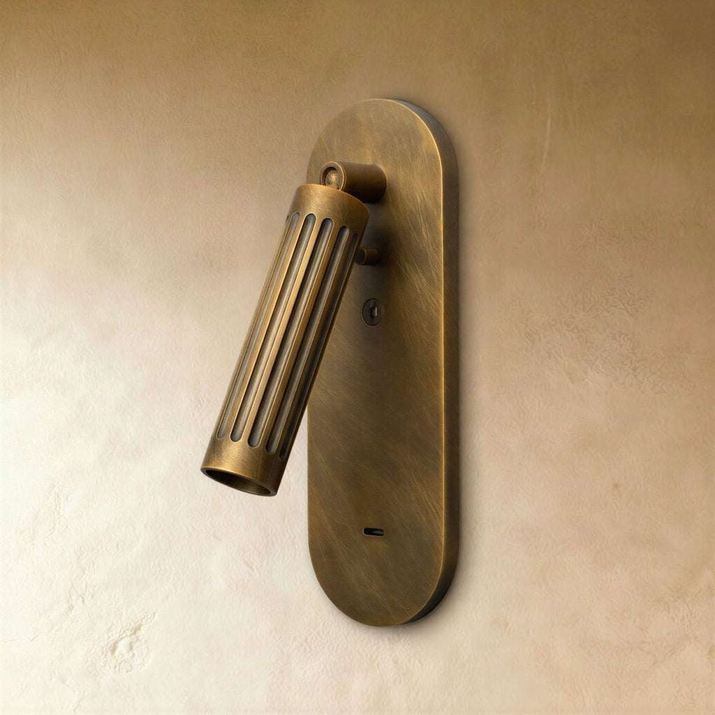 Clérachic fluted vintage brass wall light, unlit, its angled cylinder head on an oval backplate on a plaster wall