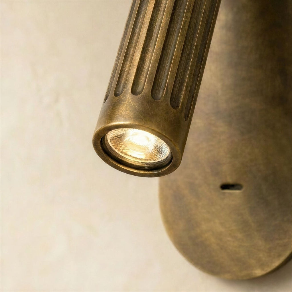 Close view of the Clérachic wall light head, a lit LED behind a fluted aged-brass cylinder, oval plate below