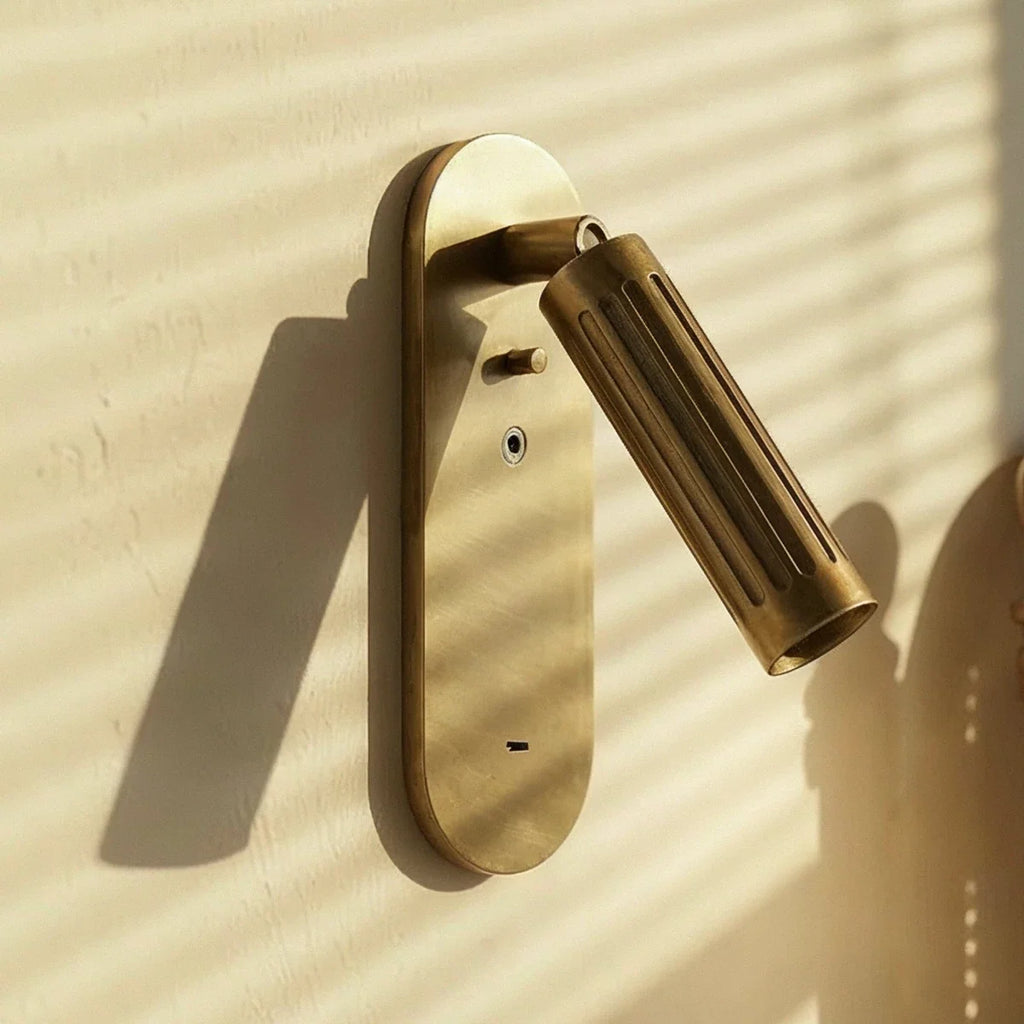 Clérachic brushed brass wall light with its fluted head angled to the right, sunlit on a pale plaster wall