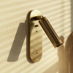 Clérachic brushed brass wall light with its fluted head angled to the right, sunlit on a pale plaster wall