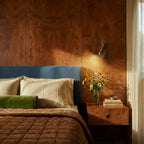 Clérachic brass reading light on a burr walnut bedroom wall above a nightstand, beside a blue headboard