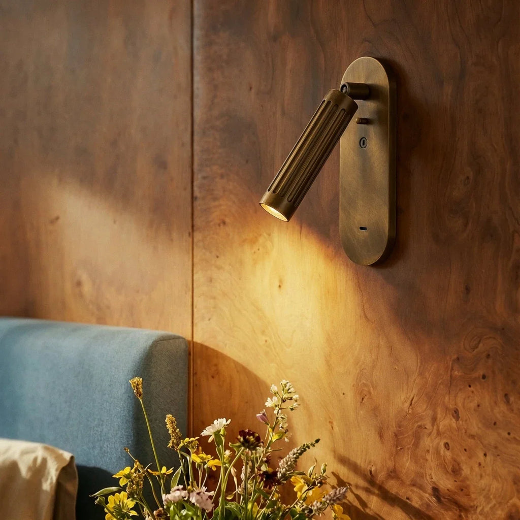 Clérachic fluted brass wall light casting a warm pool of light across a burr wood panelled wall by the bed
