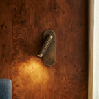 Clérachic brass wall light with its fluted head angled down, washing warm light over a burr walnut panel