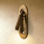 Clérachic embedded fluted brass wall light, lit, its cylinder head tilted from a recessed oval niche in the plate