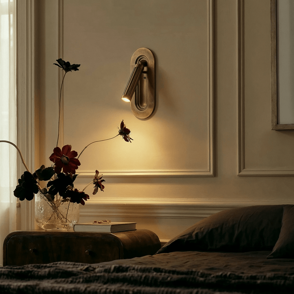Clérachic embedded brass wall light above a bedside table, lighting a panelled wall beside dark flowers