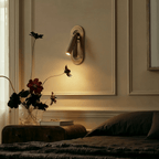 Clérachic embedded brass wall light above a bedside table, lighting a panelled wall beside dark flowers