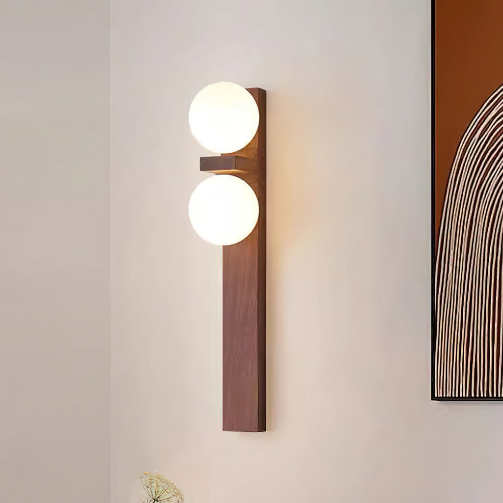 Close to a framed print, a tall Clérachic wall light with a long walnut-coloured backplate carries two lit frosted globes.