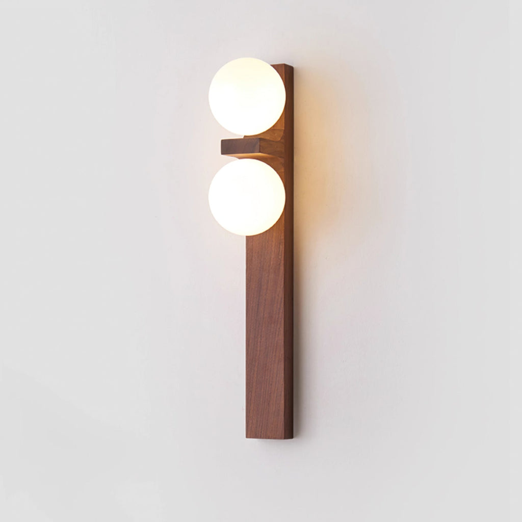 A tall Clérachic wall light with a narrow walnut-coloured backplate and two softly lit globes on a plain pale wall.