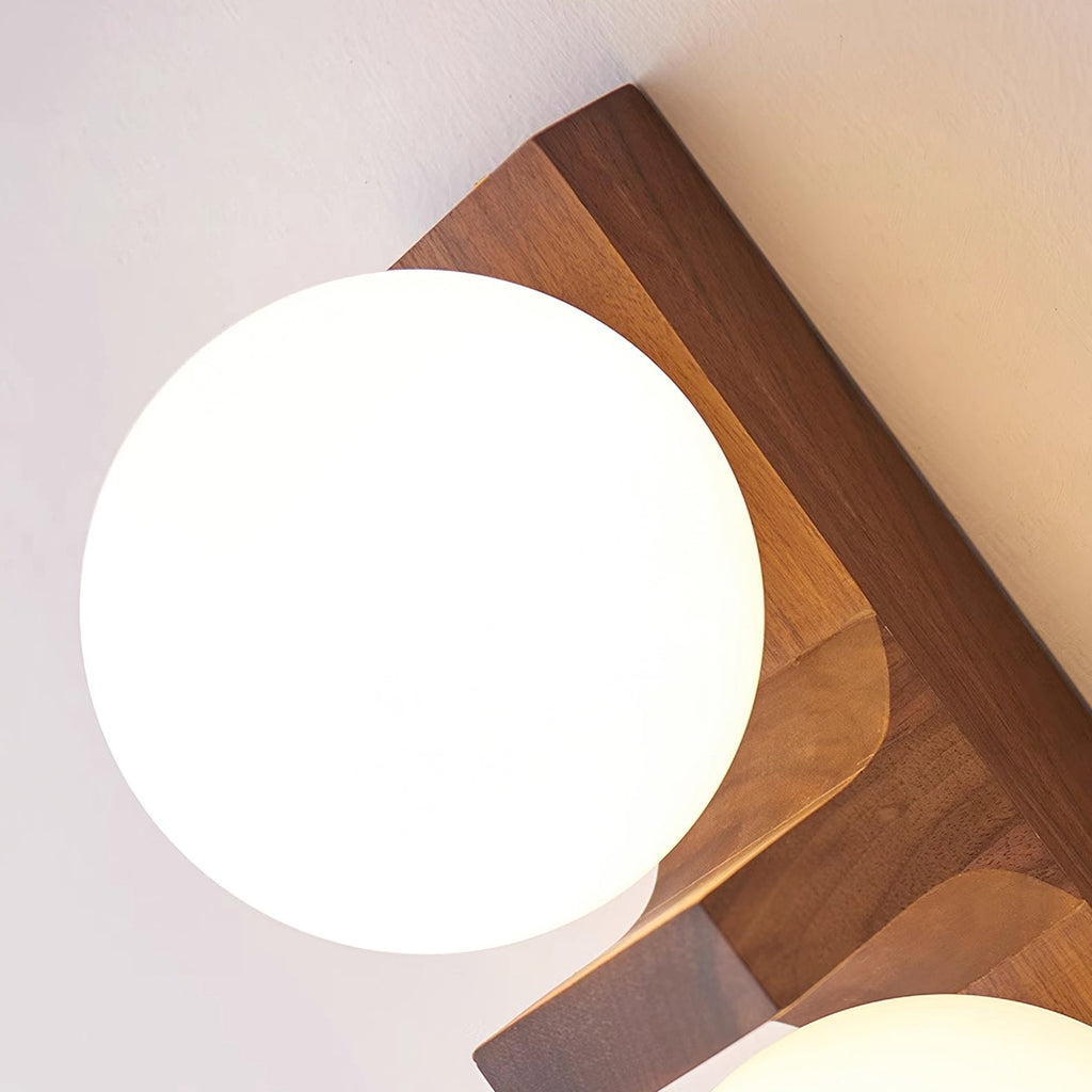Close view of a frosted white glass globe on the walnut-coloured wood bracket of this Clérachic wall light, with the grain showing.