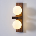 Close view of a lit Clérachic wall light, with two frosted globes on a walnut-coloured plate and a small wooden shelf between them.