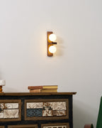 A Clérachic wall light with two glowing globes on a walnut-coloured plate hangs above a patterned cabinet with a stack of old books.