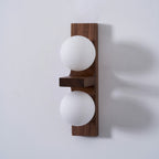 Side view of a Clérachic wall light with a walnut-coloured plate, a flat wooden shelf and two matt white globes, casting a soft shadow.