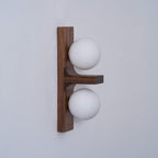 Seen from the side, a Clérachic wall light shows the grain of its walnut-coloured wood plate, a small shelf and two frosted globes.