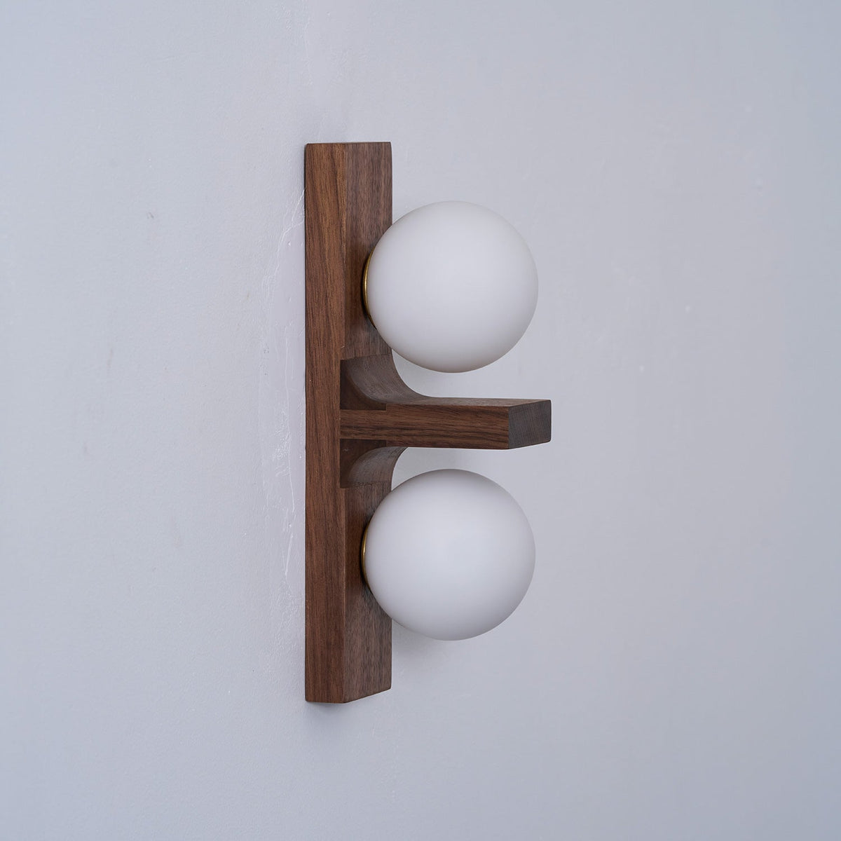 Seen from the side, a Clérachic wall light shows the grain of its walnut-coloured wood plate, a small shelf and two frosted globes.