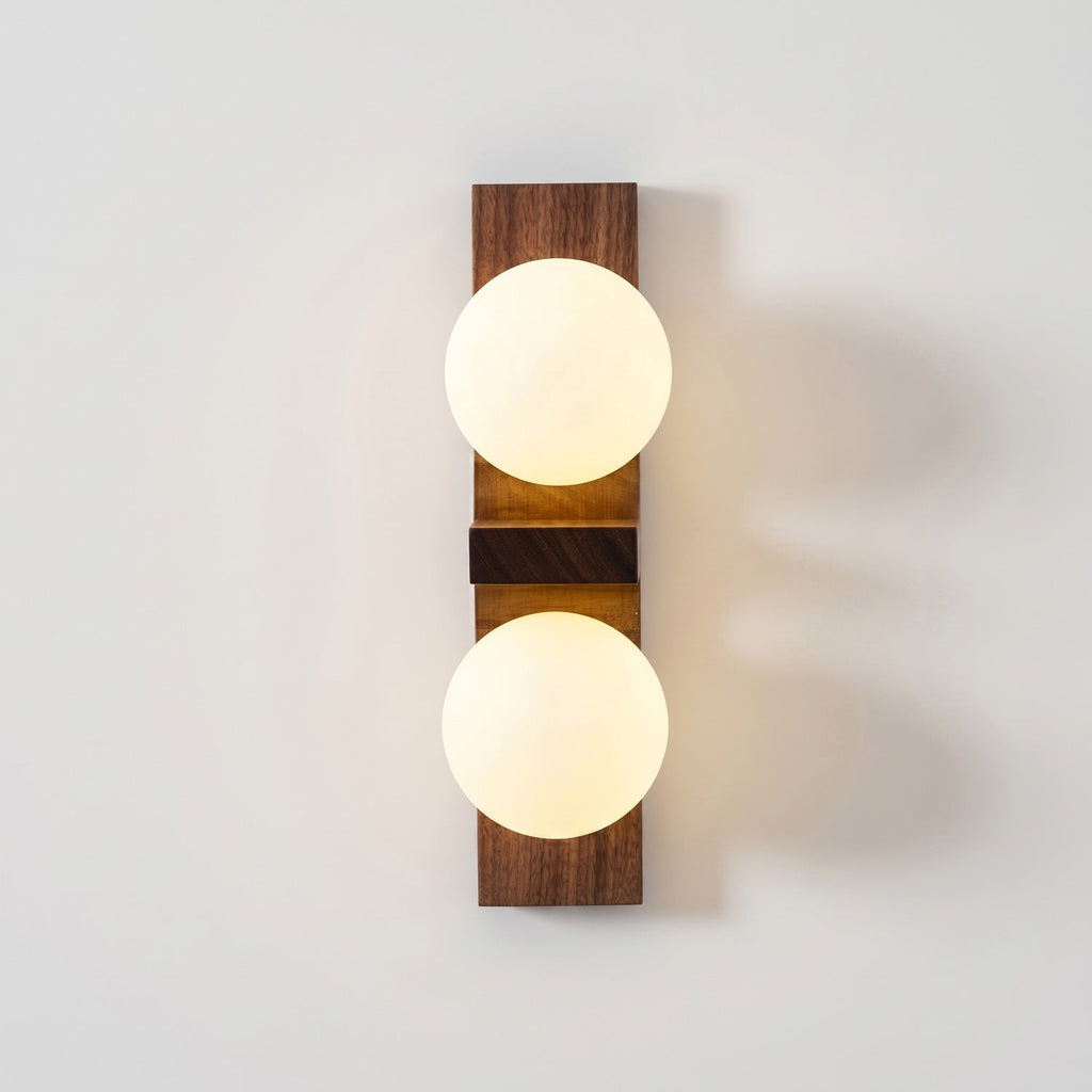A Clérachic wall light with two bright frosted globes and a darker walnut-coloured plate casts a warm glow on a white wall.