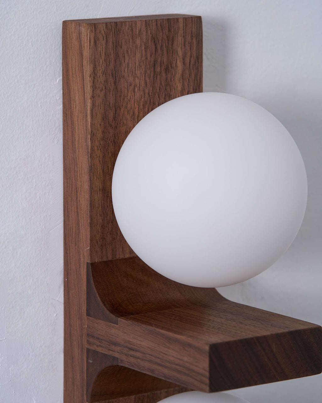 Close view of one frosted white globe resting on the curved wooden bracket of this Clérachic wall light.