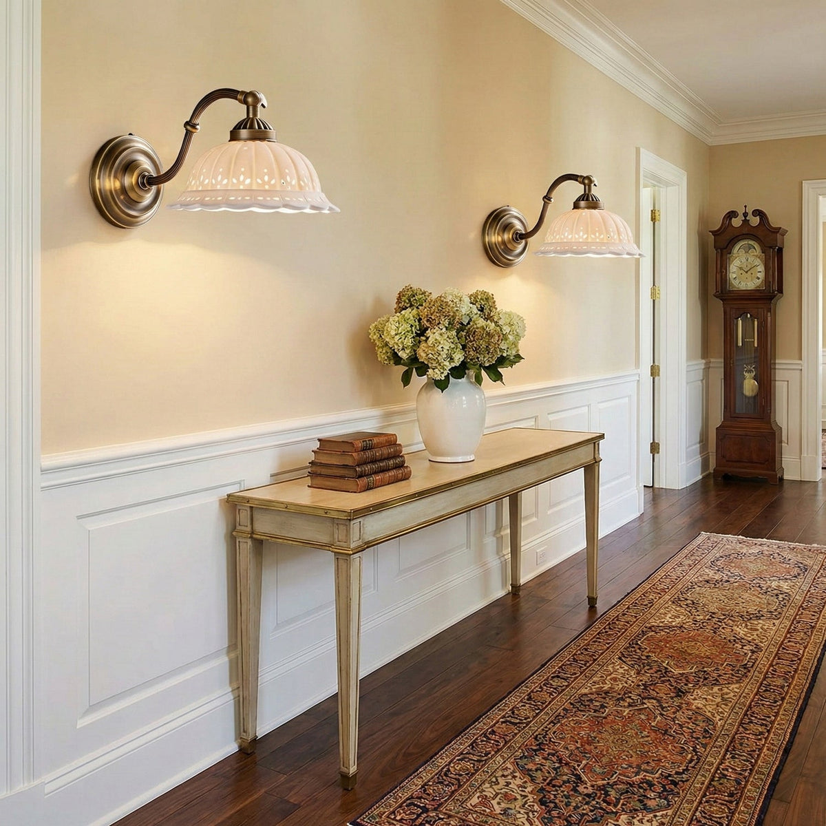 Two lit Clérachic wall lights with pierced ceramic shades hang above a console table in a hallway with white panelling and a runner rug.