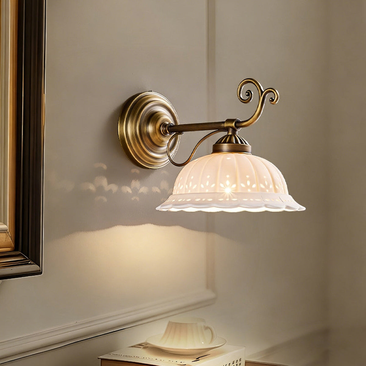 Small patterns fall on the wall from a Clérachic wall light whose straight brass arm ends in a scroll and holds a white ceramic shade.