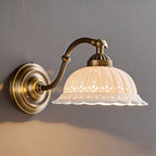 Warm light pools on a grey wall from a Clérachic wall light with a curved brass arm and a ribbed white ceramic shade.