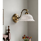 An unlit Clérachic wall light with a white ceramic shade pierced with small holes hangs in a corner above a vase of flowers.