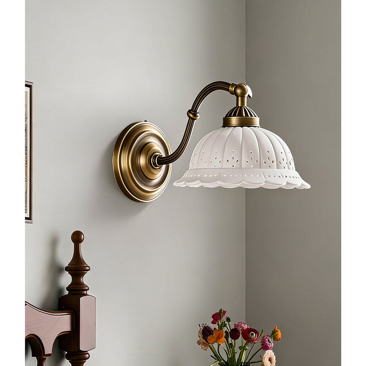 An unlit Clérachic wall light with a white ceramic shade pierced with small holes hangs in a corner above a vase of flowers.