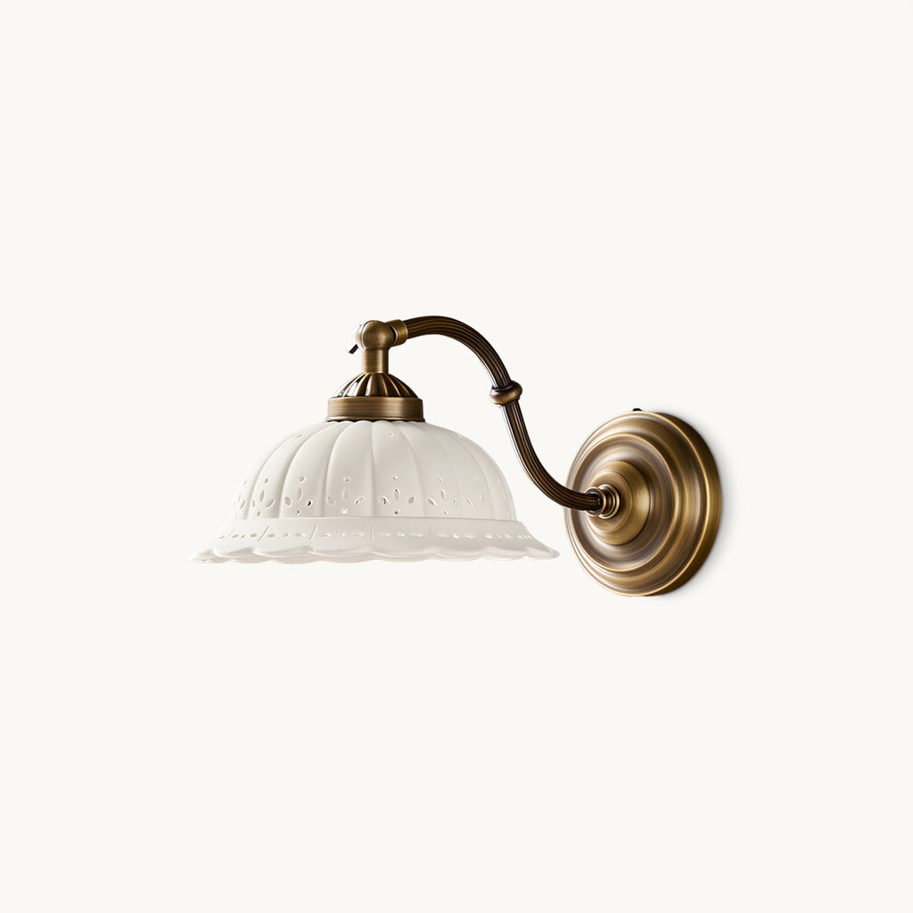 On a plain white backdrop, an unlit Clérachic wall light shows a pierced white ceramic shade, a curved antique brass arm and a round backplate.