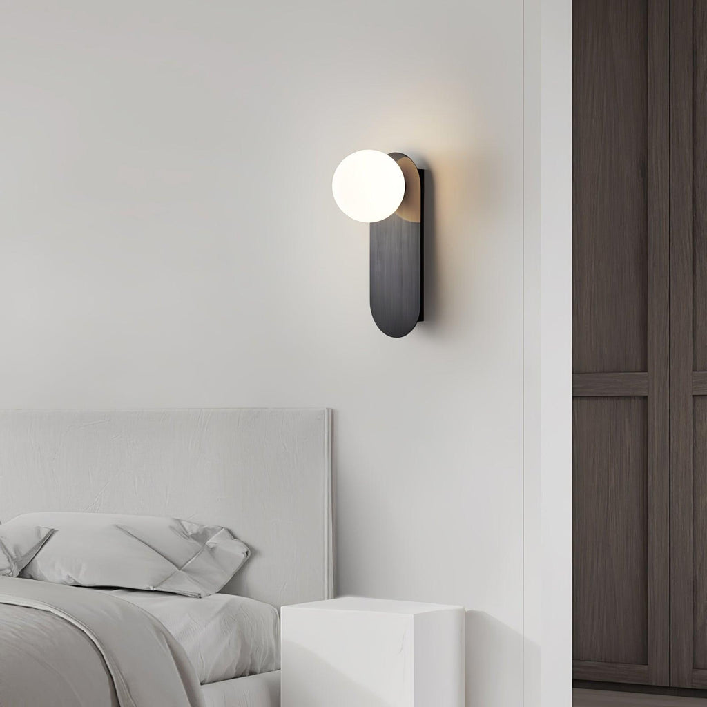 Black-finish globe wall light from Clérachic beside a white upholstered headboard and a dark wardrobe door.