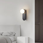 Black-finish globe wall light from Clérachic beside a white upholstered headboard and a dark wardrobe door.