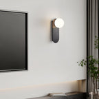 Black globe sconce from Clérachic beside a wall-mounted dark television, with a tall plant and a curtain at the edge.