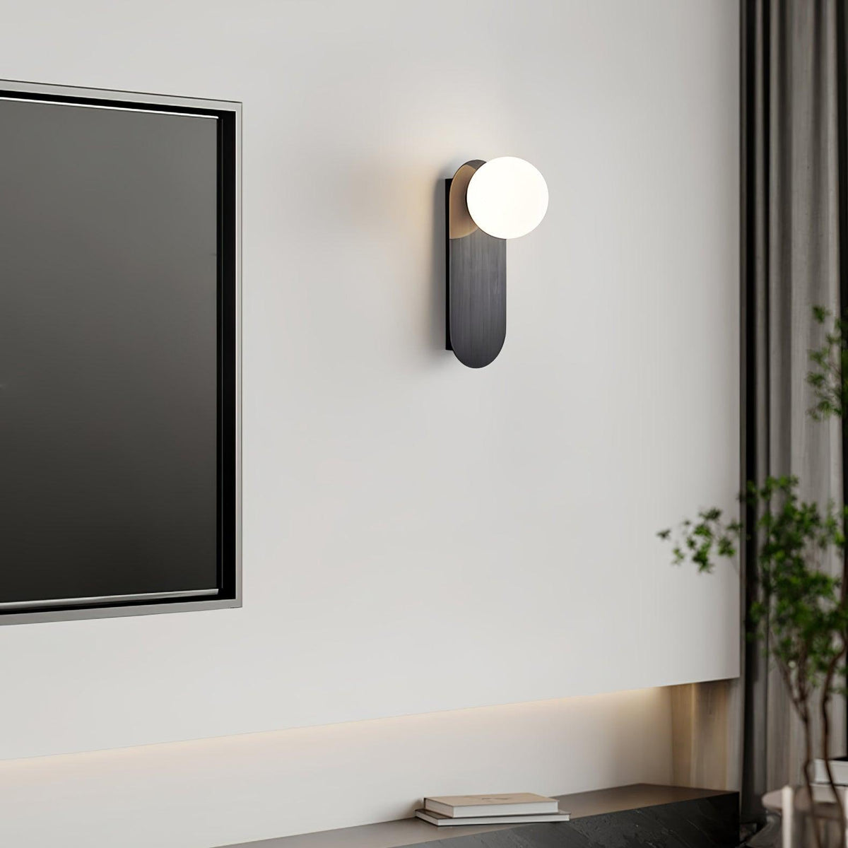 Black globe sconce from Clérachic beside a wall-mounted dark television, with a tall plant and a curtain at the edge.