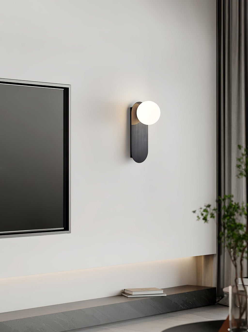Narrow black Clérachic wall light with a white globe next to a framed screen, above a low shelf with a book.