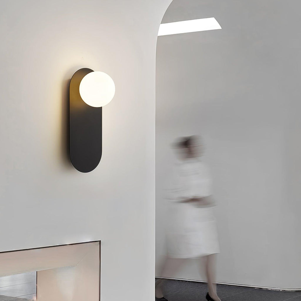 Lit black globe sconce from Clérachic by an arched opening, with a blurred figure in white walking past.