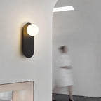 Lit black globe sconce from Clérachic by an arched opening, with a blurred figure in white walking past.