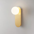 Close view of a brass globe wall light from Clérachic on a soft grey wall, the white globe sitting at the top of the plate.