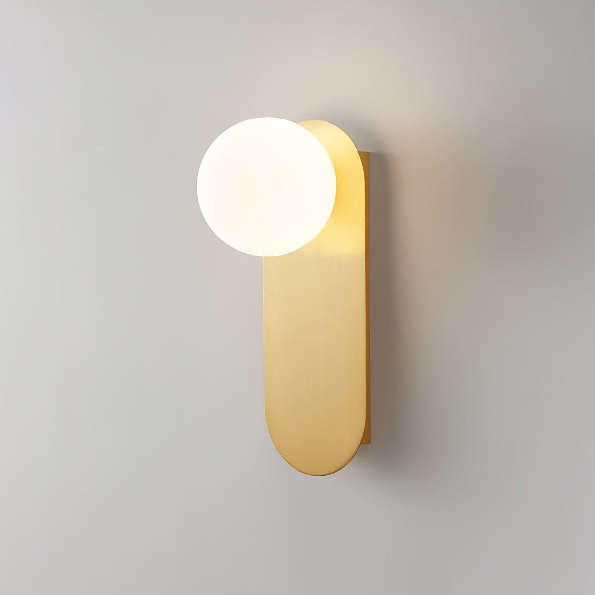 Close view of a brass globe wall light from Clérachic on a soft grey wall, the white globe sitting at the top of the plate.