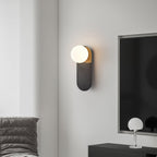 Black Clérachic globe sconce on a grey wall next to a dark screen, with a small glass-ball lamp on a console below.