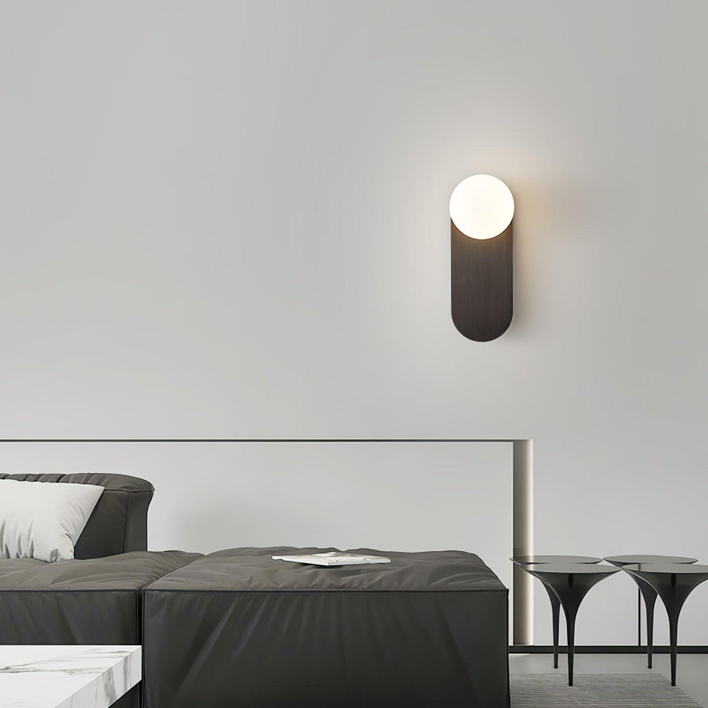 Lit black globe wall light from Clérachic high on a pale wall above a charcoal sofa and glass-topped side tables.