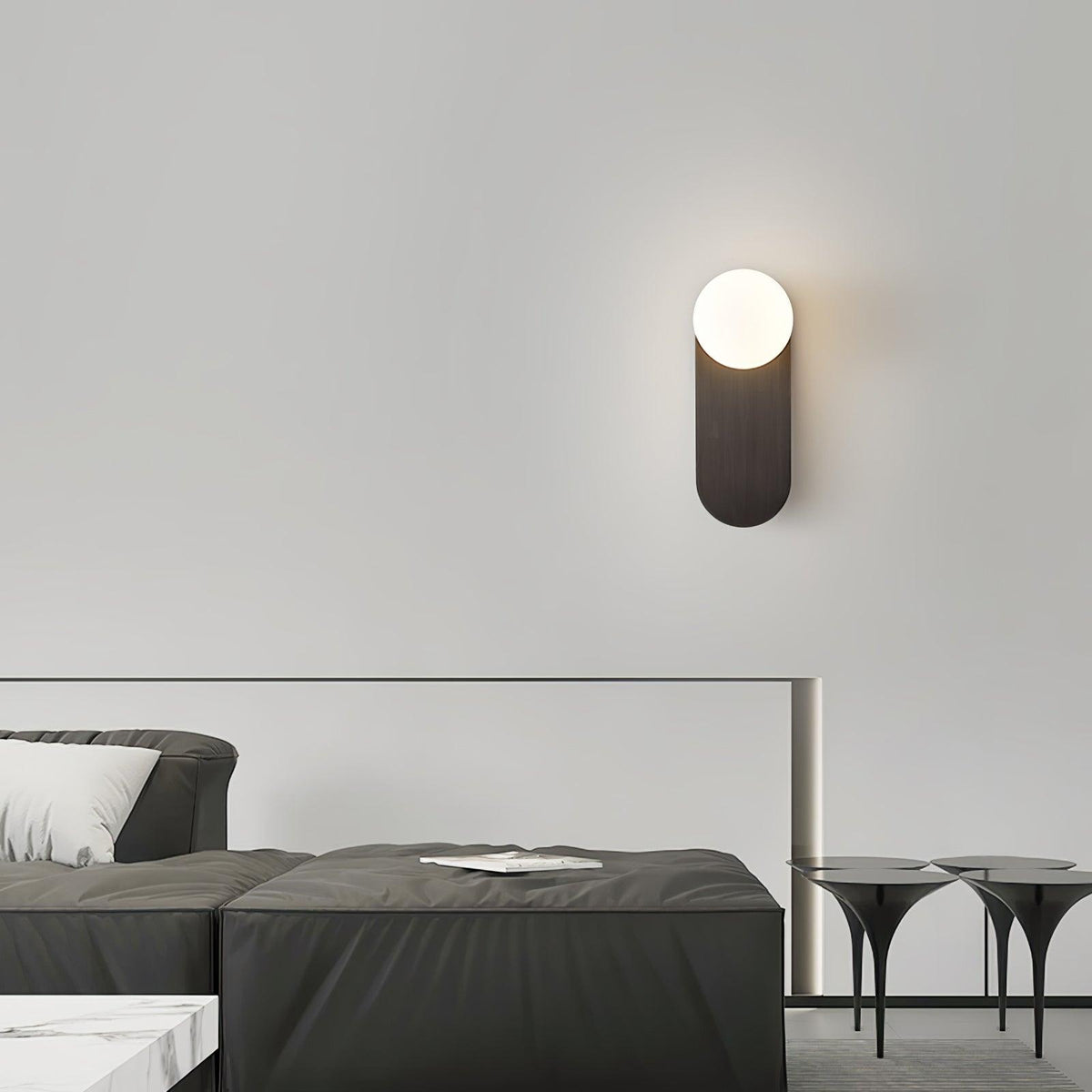 Lit black globe wall light from Clérachic high on a pale wall above a charcoal sofa and glass-topped side tables.