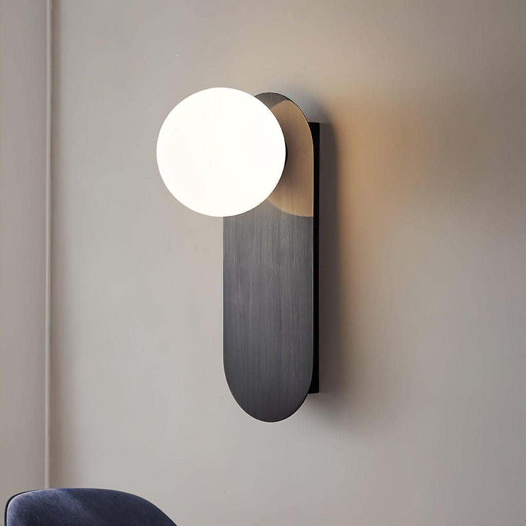 Close view of the black brushed plate and white globe of this Clérachic wall light, with warm light on the wall behind.