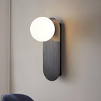 Close view of the black brushed plate and white globe of this Clérachic wall light, with warm light on the wall behind.