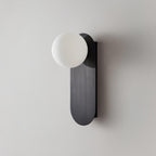 Unlit white frosted globe on a black brushed plate, this Clérachic wall light shown close on a light grey wall.