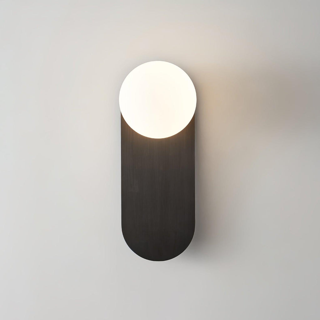 Close view of the black brushed plate and lit white globe on this Clérachic wall sconce on a pale grey wall.