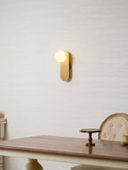 Lit brass Clérachic globe wall light on a textured cream wall above a wooden table with a small cake stand.