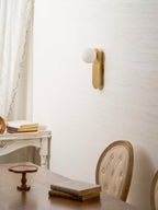 Brass Clérachic globe sconce above a wooden table with a book and a small wooden tray, with a chair at the edge.