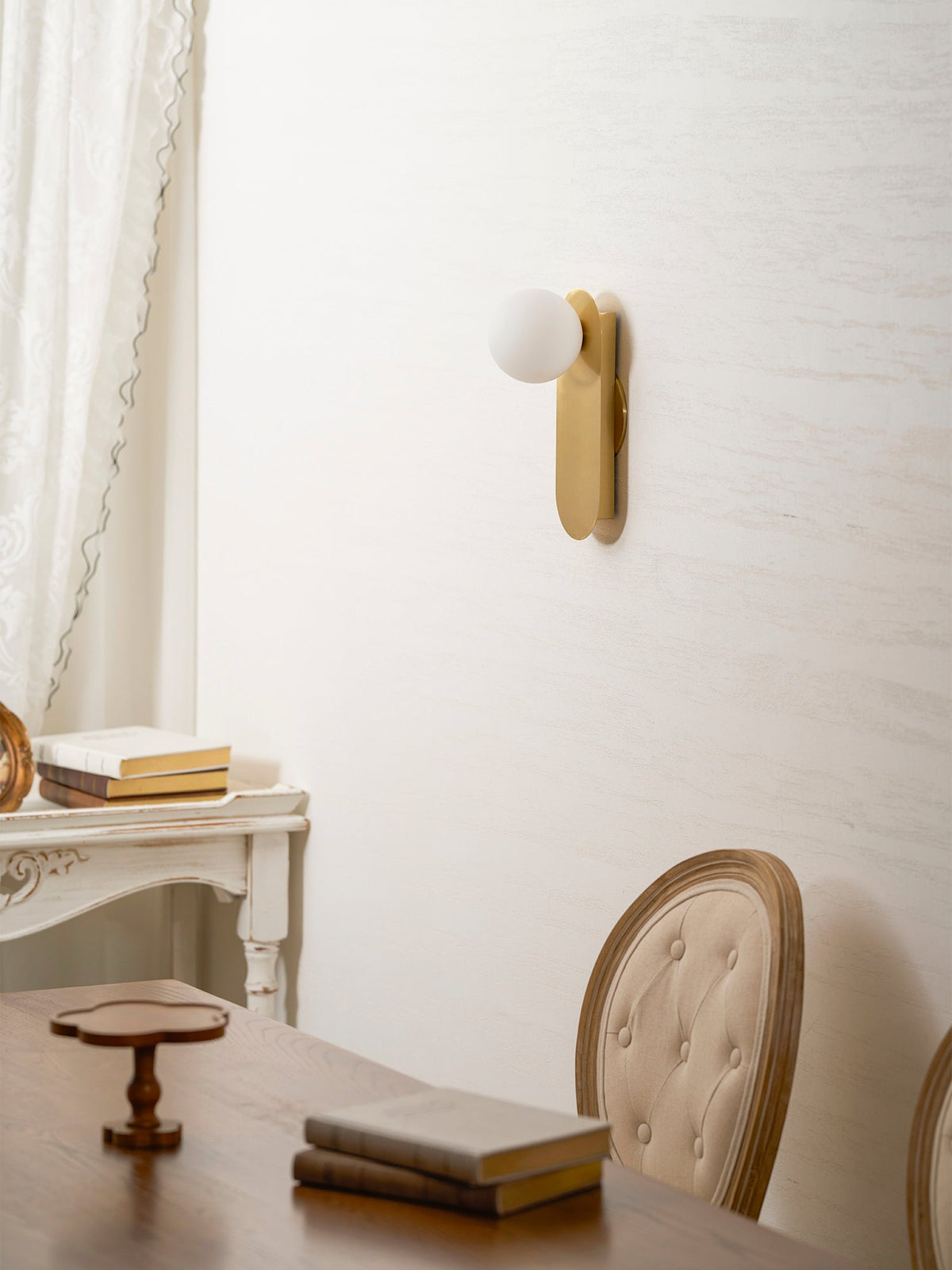 Brass Clérachic globe sconce above a wooden table with a book and a small wooden tray, with a chair at the edge.