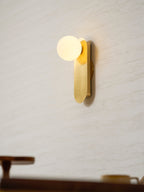 Lit brass globe sconce from Clérachic glowing on a cream wall, with a blurred table and cup at the bottom of the frame.