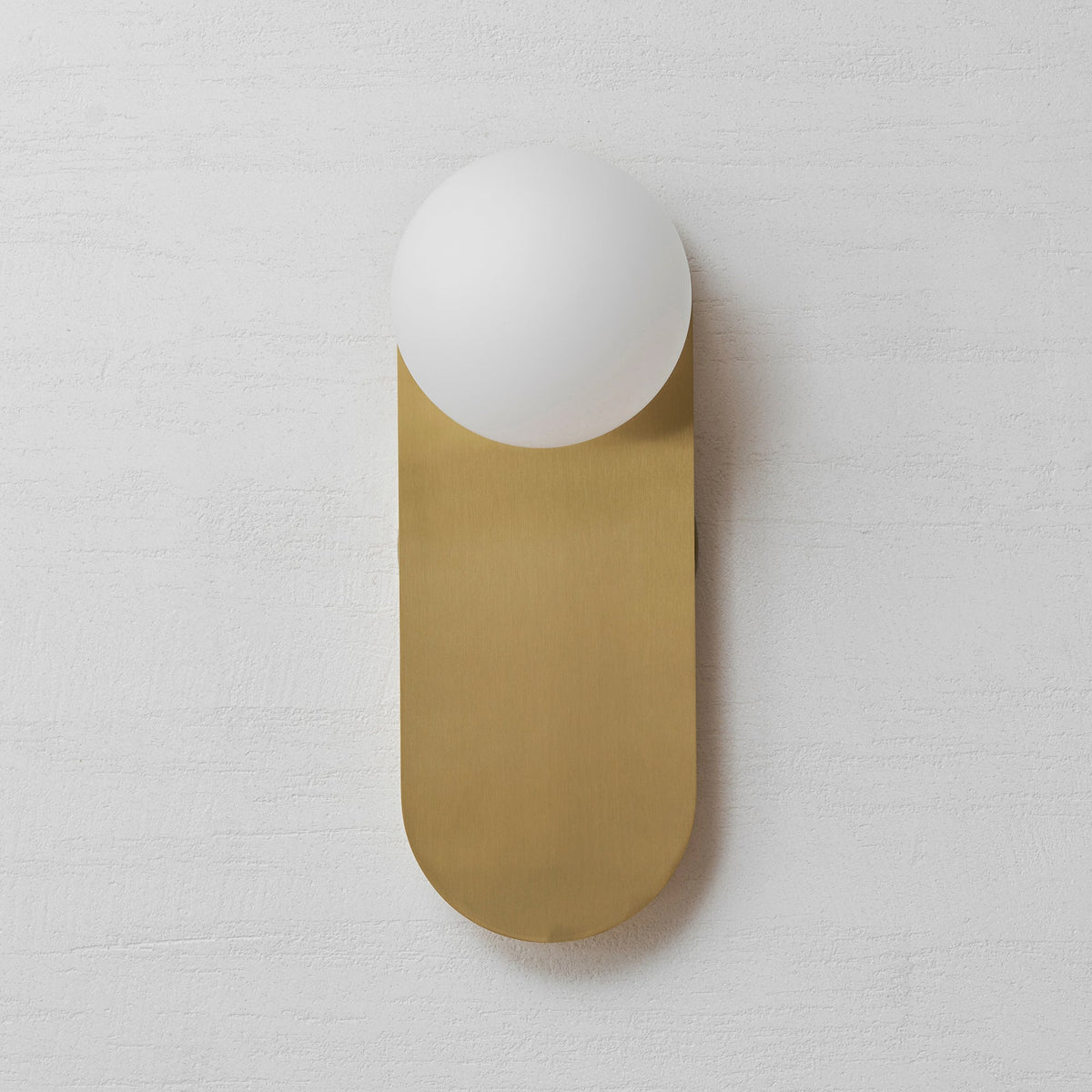 Front view of the brushed brass plate and white globe of this Clérachic wall light on a pale textured wall.